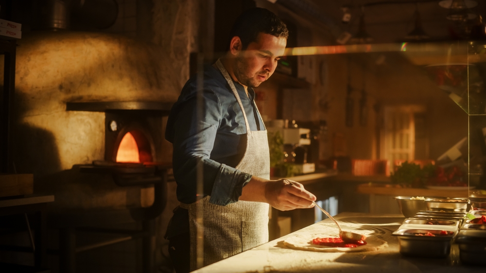 GV Compta - Un pizzaiolo préparant une pizza dans une pizzeria, représentant les clients de GV Compta dans le secteur de la restauration. L'image illustre l'accompagnement comptable pour les entreprises de ce domaine, de la gestion de la comptabilité à l'optimisation fiscale.